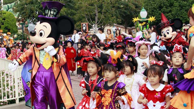 Children in Halloween costumes stand next to Mickey Mouse at Tokyo Disneyland.