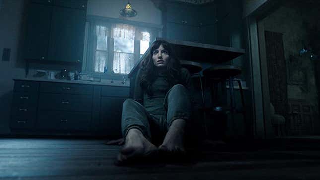 A frightened woman sits on the floor of a dark kitchen in James Wan's new horror movie, Malignant.