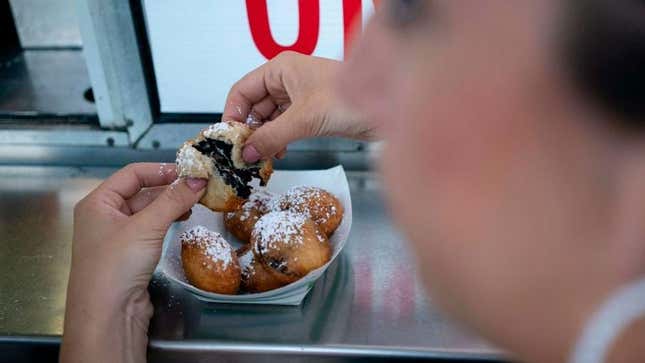 Hands pulling apart a deep-fried Oreo over a paper boat full of fried Oreos