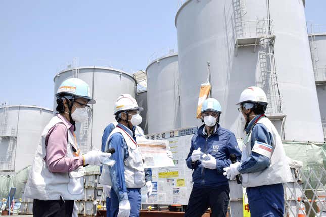 Four men in hard hats, masks, and gloves talking outside at the Fukushima Daiichi nuclear power plant.