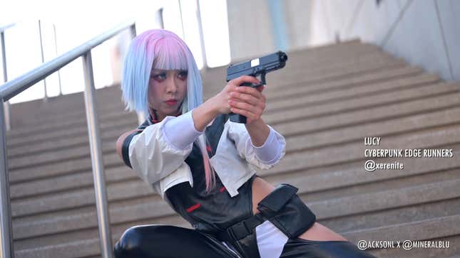 A cosplayer dressed as Lucy from Cyberpunk: Edgerunners crouches down with a pistol in their hand. 