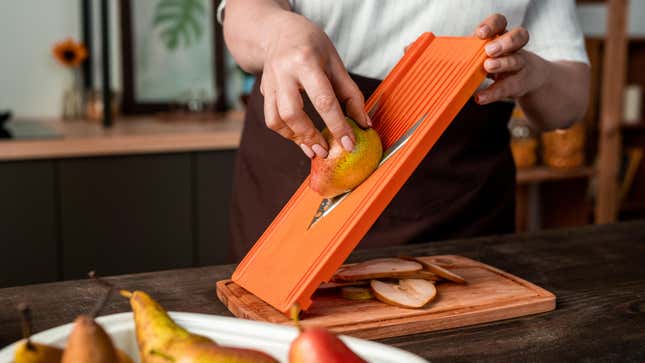 A chef is seen using a mandoline slicer to cut thin slices of pear