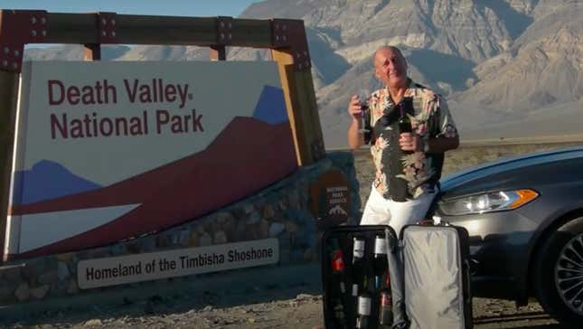 Man holds up glass of wine in front of "Death Valley National Park" sign