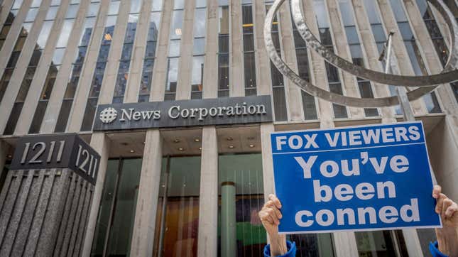 Participant seen holding a sign outside Fox News HQ that reads "Fox viewers: You've been conned"