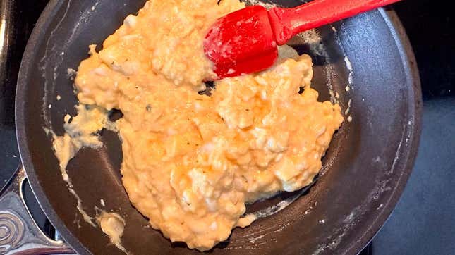 Scrambled eggs in a pan with a red spatula.