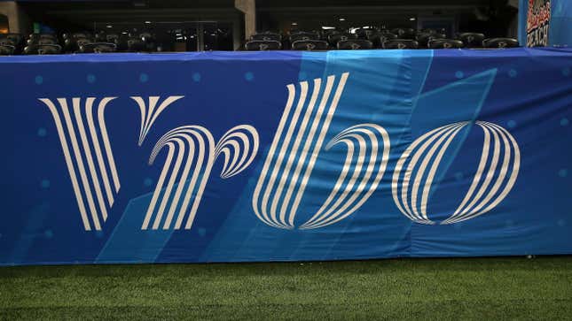 The Vrbo logo on a blue sheet in front of a football field.