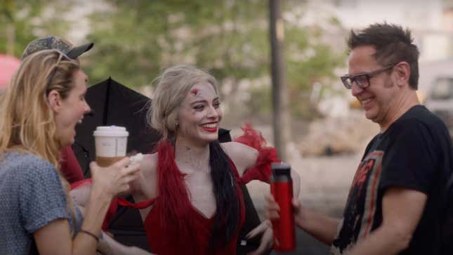 James Gunn laughs with Margot Robbie, playing Harley Quinn, in a tattered red dress.