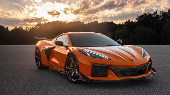 Orange Corvette parked in front of trees.