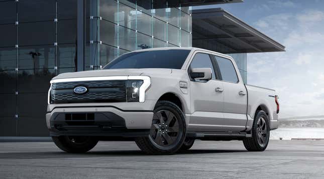 A light gray 2023 Ford F-150 Lightning is parked in front of a glass building.