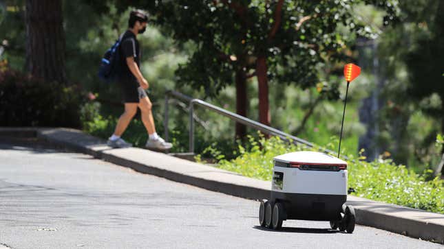 A white delivery robot driving along an empty road. 