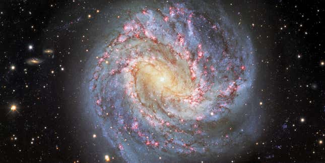 A spiral galaxy shines in yellow, blue, and pink light.