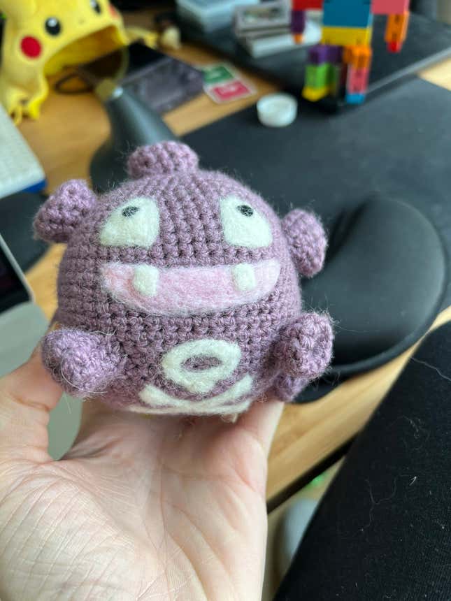 A hand is shown holding a crochet Koffing.