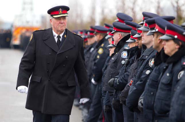 Toronto police chief Bill Blair walks by officers lining the roadway at the public memorial for a police constable on December 9, 2013.