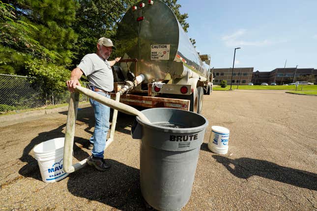 Ty Carter with Garrett Enterprises, fills up a large garbage can with non-potable water in the Forest Hill High School parking lot in Jackson, Miss., Wednesday, Aug. 31, 2022. The tanker is one of two placed strategically in the city to provide residents non-potable water. The recent flood worsened Jackson’s longstanding water system problems and the state Health Department has had Mississippi’s capital city under a boil-water notice since late July.