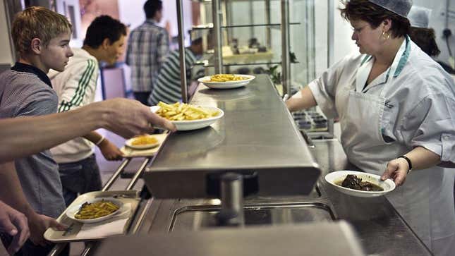 Line of students picking up plates of food handed off by cafeteria worker
