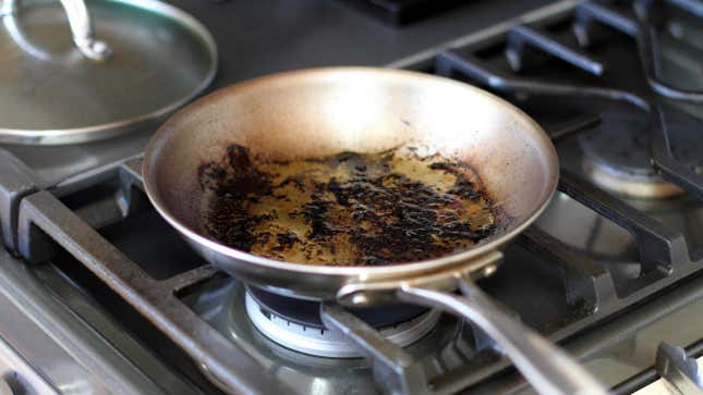 A frying pan coated in charred grease sits on a burner on a stovetop