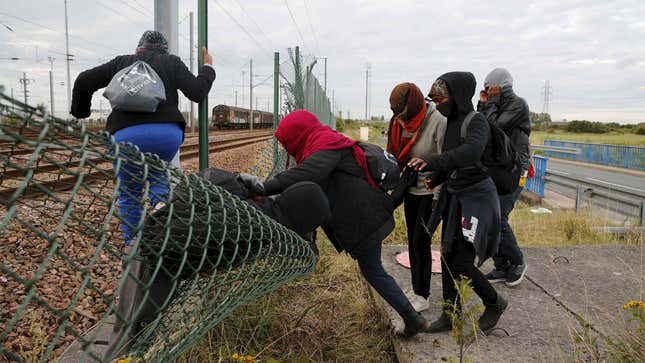 Migrants make their way across a fence near train tracks as they attempt to access the Channel Tunnel in Frethun, near Calais