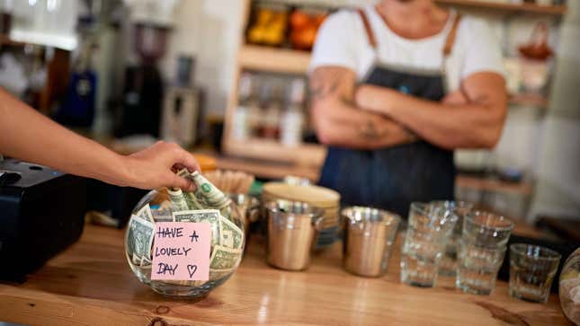 Person adding a dollar to a tip jar in coffee shop