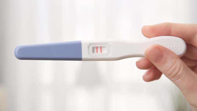 A hand holds up a home pregnancy test displaying two pink lines