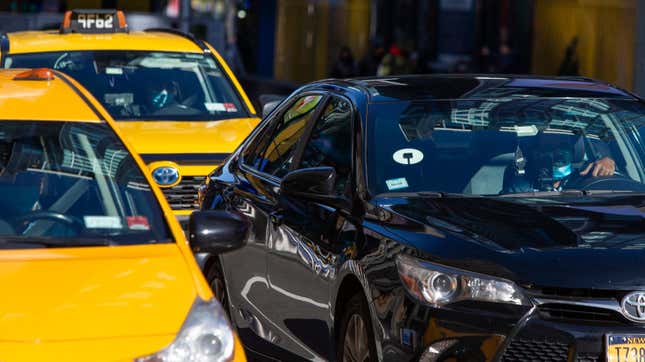 Yellow cabs and Uber car drive through Times Square on November 16, 2020 in New York City. NYC bill is looking to put Uber and yellow Cabs on single app platform where riders order from the app any for-hire vehicle, including taxis and cars of Uber or Lyft.