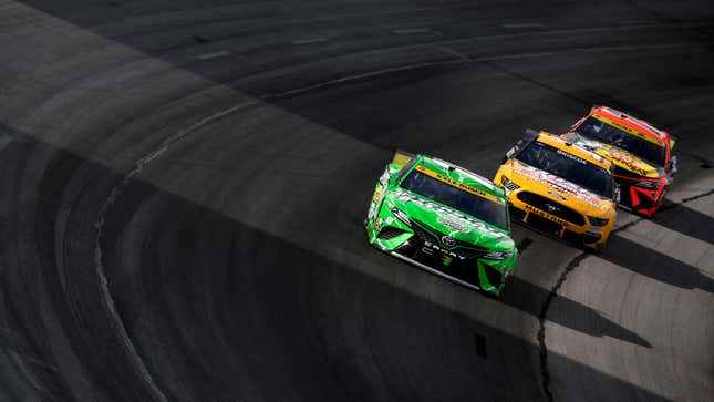 Three NASCAR cars racing on a banked turn. 
