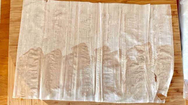 A sheet of phyllo dough on a cutting board. The bottom-half has been lightly buttered.