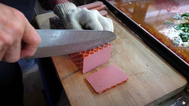 Knife slicing block of processed meat