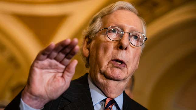 An older man with a prominent neck and jowls holds up his hand.