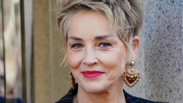 Sharon Stone smiles wearing large, heart shaped earrings.