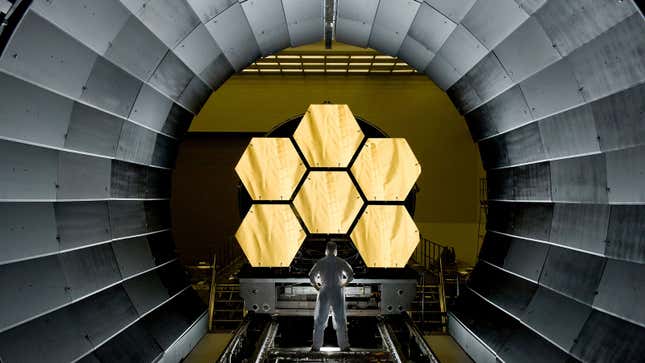 An engineer stands in front of six of the James Webb Space Telescope's mirrors