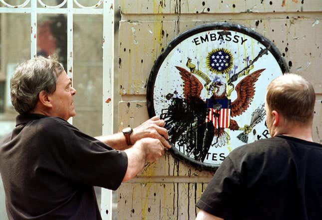Two men remove the battered insignia from the gate of the US embassy in Beijing on May 12, 1999.