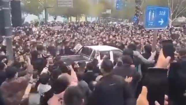 A crowd of people with cell phones surround a white pickup truck.