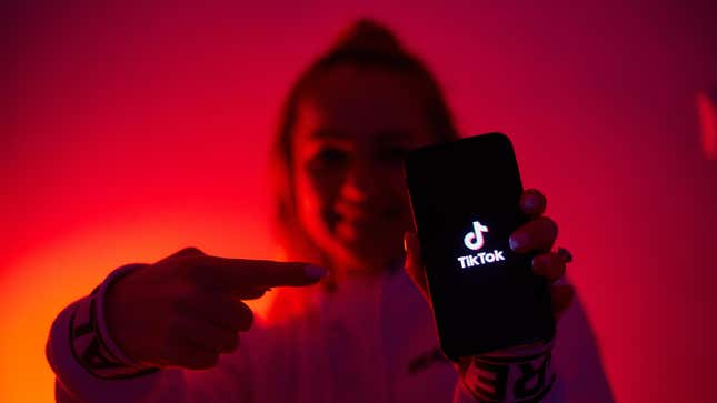 An image of a girl pointing to her phone, which has the TikTok app open.