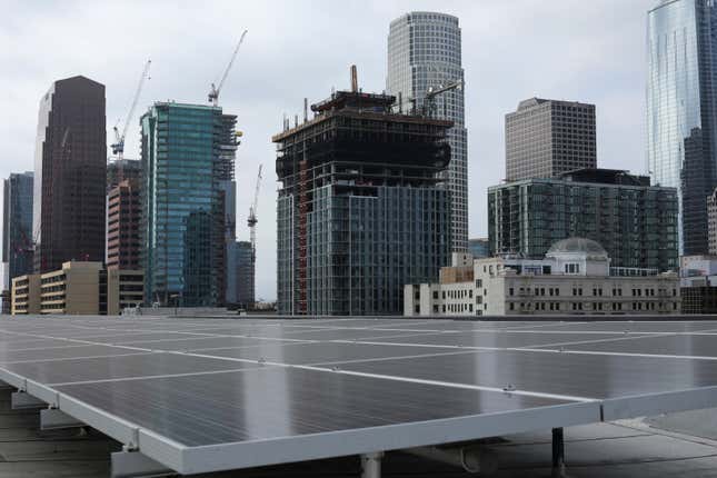 solar panels are seen in the foreground, in the background are skyscrapers in downtown Los Angeles