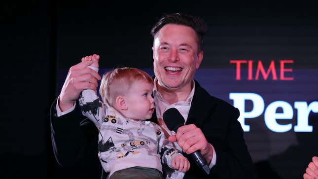 Elon Musk holds his son X Æ A-12's hand on stage at an event.
