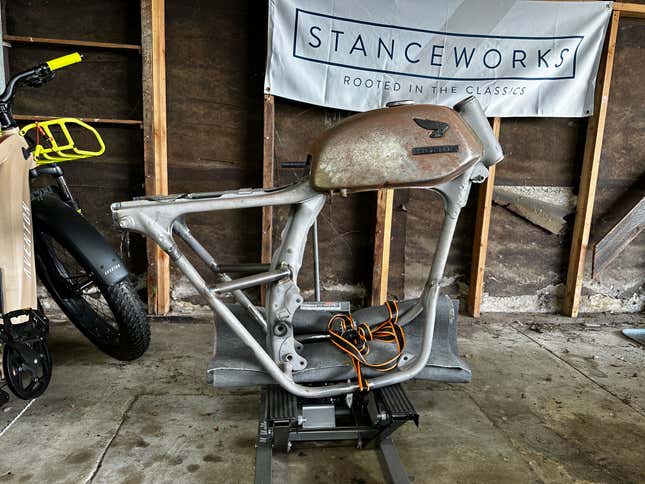 A bare motorcycle frame with a gas tank is on a motorcycle lift in a garage.