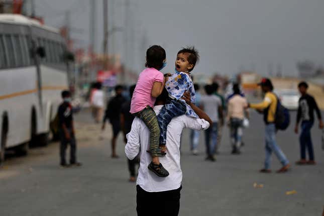 An Indian man carries his children on his shoulders as he along with his family walk along an expressway hoping to reach their home, hundreds of miles away, as the city comes under lockdown in Ghaziabad.