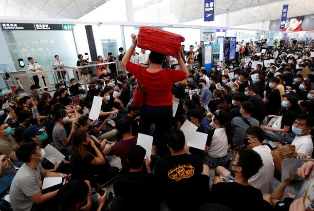 A passenger walks past protesters sitting on the floor in front of security gates during a demonstration at Hong Kong airport, Aug. 13, 2019.