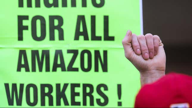 A fist is raised in front of a green sign that says "RIGHTS FOR ALL AMAZON WORKERS!"