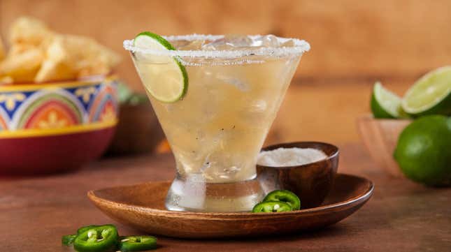 Margarita glass on table with jalapeno slices, lime, and tortilla chips