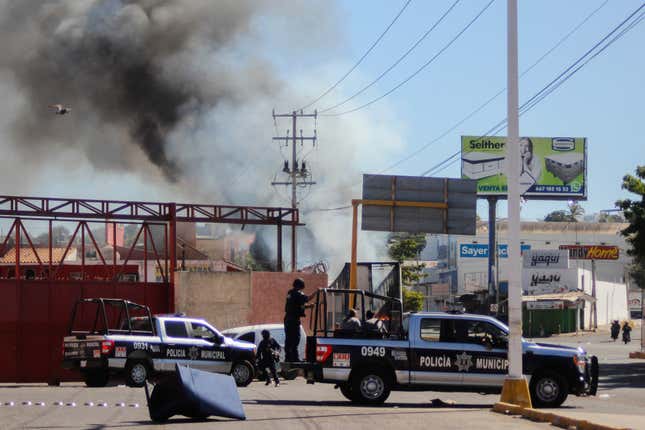 Varias camionetas de la policía se agrupan con un incendio de fondo en Culiacán.
