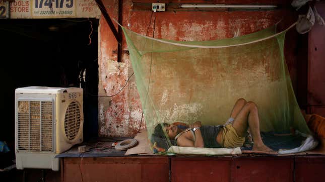 An Indian migrant daily wage worker sleeps next to an air cooler under a mosquito net on a steel box, used to store items of shop at night, in New Delhi.
