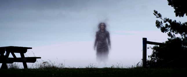 An otherworldly woman emerges from the mist behind a fence and a picnic table.