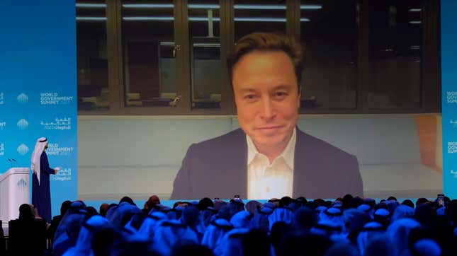 Elon Musk tunes in to the World Government Summit in 2023 as a crowd of spectators look on.