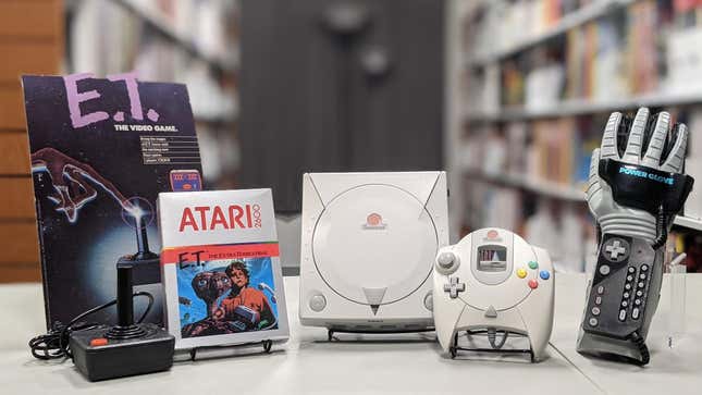 A pile of gaming relics, including the Dreamcast and E.T., sit on a table at the Museum of Video Game History.
