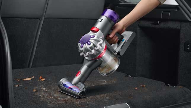 A Dyson vacuum being used to suck up dirt in the back of a vehicle.