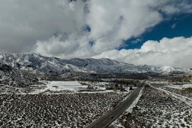 Clouds hover over snow-covered mountains as a car drives along a state route near Phelan, California on Wednesday, March 1, 2023.