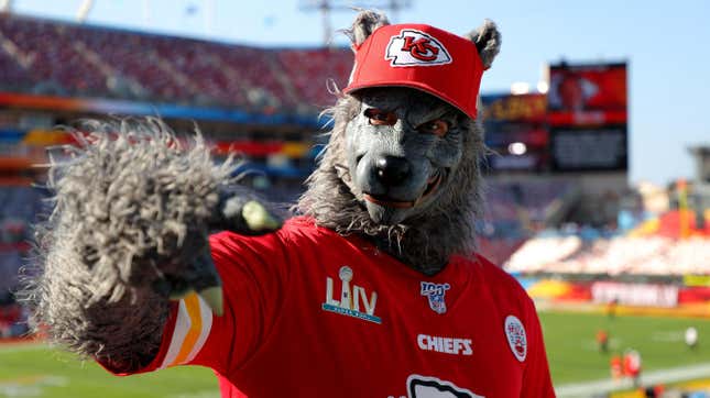 A man in a ratty wolf costume, wearing a Kansas City Chiefs jersey and hat, points at something in Arrowhead Stadium.