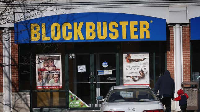 A Blockbuster storefront with movie posters Looper and the Paperboy in front of it.