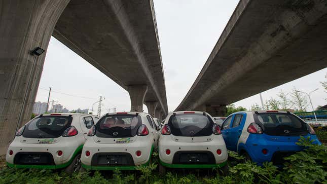 A photo of four small electric cars abandoned under a bridge. 